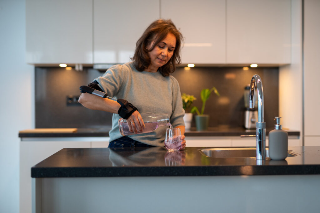 Für wen eignet sich die Stil Hand Control™? Tremor, Alltag und Beratung bei Kurda in Kiel 1 Frau trägt die Stil Hand Control Orthese und schenkt sich Wasser ein.
