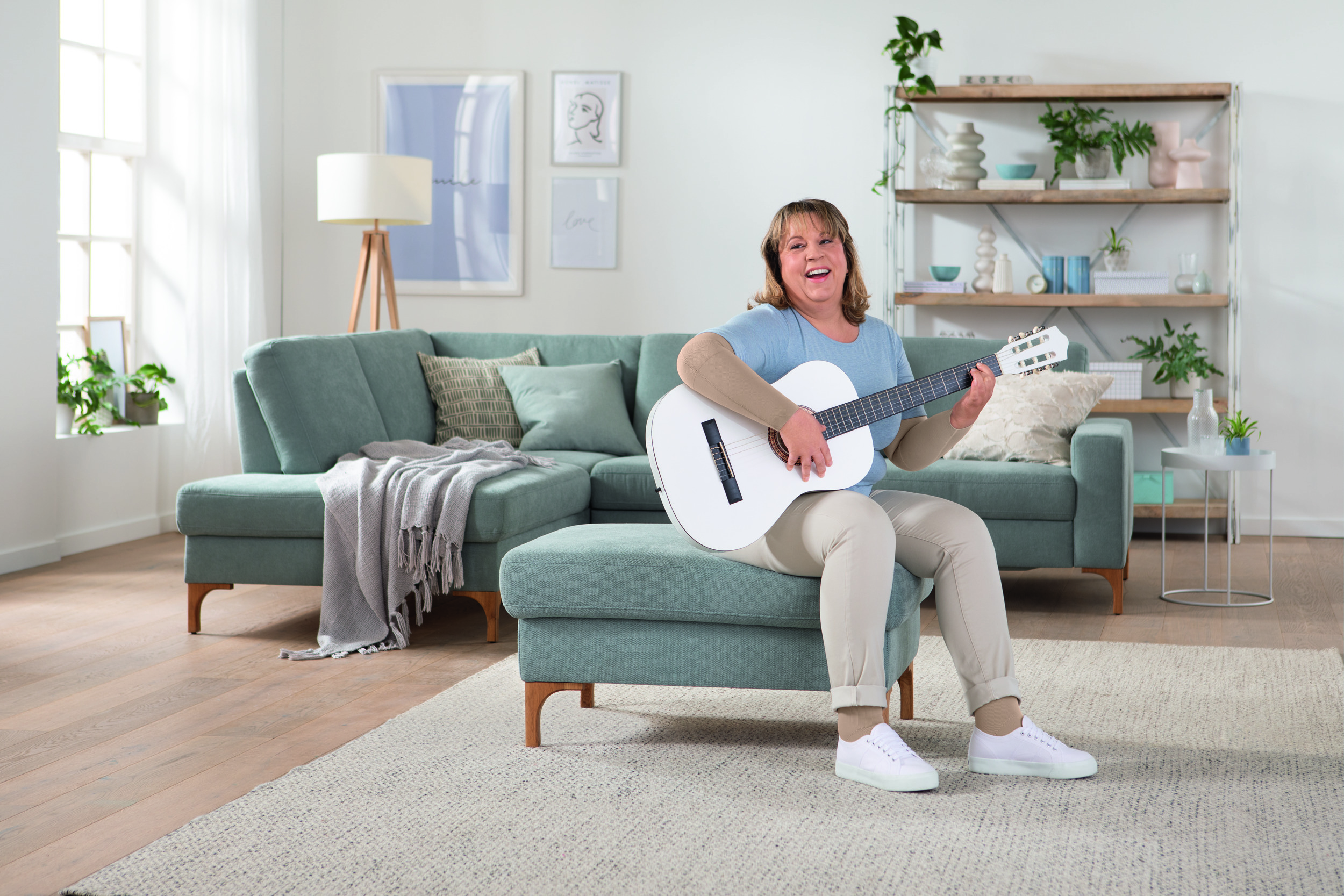Frau mit Gitarre trägt einen Kompressionsarmstrumpf und sitzt auf einem Sofa.