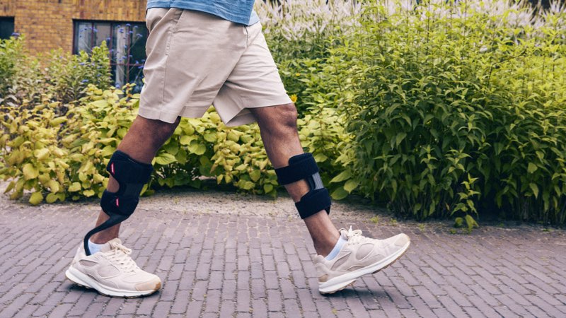 Person geht sicher mit Fußheberorthesen (Carbon-Unterschenkelorthesen) über einen gepflasterten Gartenweg